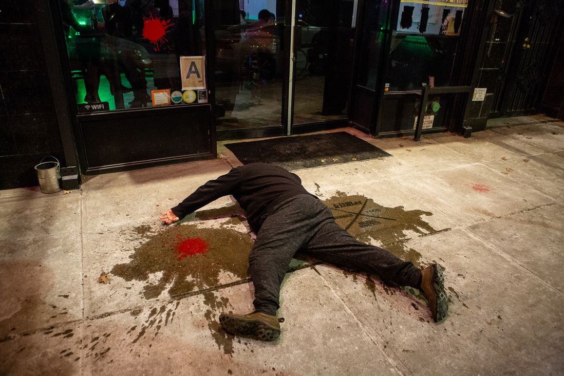 A man plays dead outside the bar, which has been painted with "blood wound splatters"